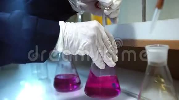 手套中的手在实验室的烧瓶中混合粉红色液体和黄色液体视频的预览图