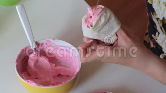 一个女人把粉红色的奶油放进糕点袋里下一个海绵蛋糕铺上白色奶油视频的预览图