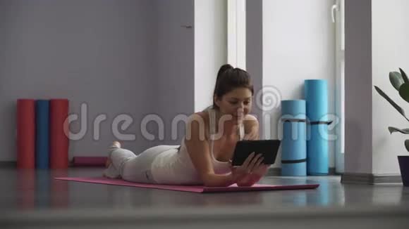 女孩躺在瑜伽垫上看着平板电脑视频的预览图