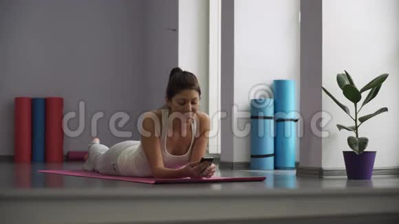 女人躺在瑜伽垫上看着电话视频的预览图
