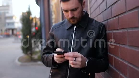 一个年轻人用智能手机站在城市的砖墙边视频的预览图