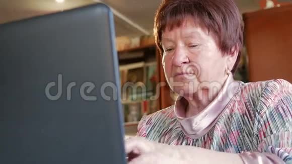 一位年长的妇女在家里用笔记本电脑检查社交网络上的信息她坐在桌边视频的预览图