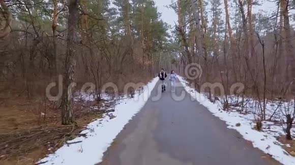 两个年轻的朋友在冬天的森林里沿着这条路跑视频的预览图