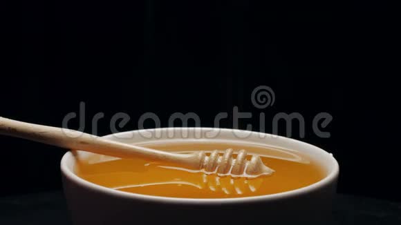 在黑色背景下分离的碗中加入蜂蜜的蜜盘视频的预览图