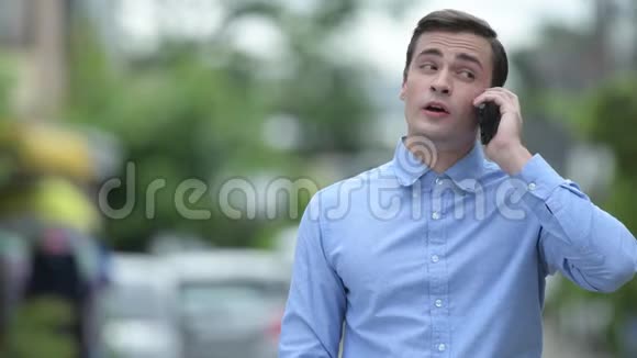 年轻快乐英俊的商人一边在户外打电话一边思考视频的预览图