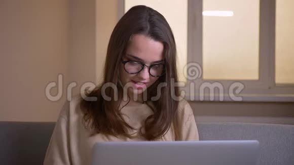 一位年轻漂亮的白种人女商人戴着眼镜在办公室的室内电脑上打字视频的预览图