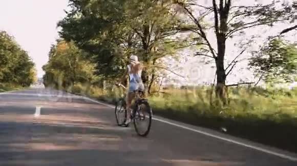一个年轻的金发女孩穿着复古自行车在田野的路上走视频的预览图