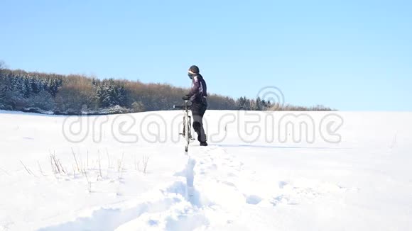 一个骑着山地车的人比克正在雪地里推自行车多云的冬日风和雪花轻柔视频的预览图