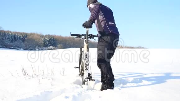 一个骑着山地车的人比克正在雪地里推自行车多云的冬日风和雪花轻柔视频的预览图