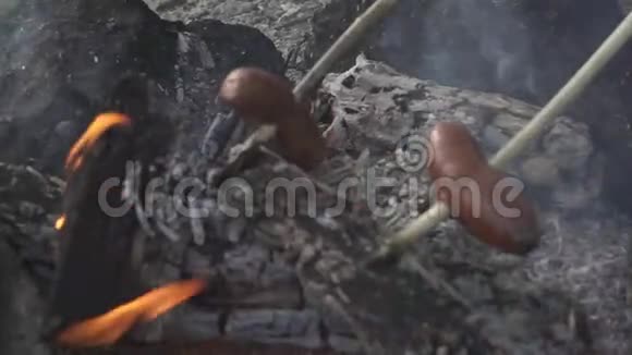 两根连在棍子上的香肠正在篝火上烤着视频的预览图