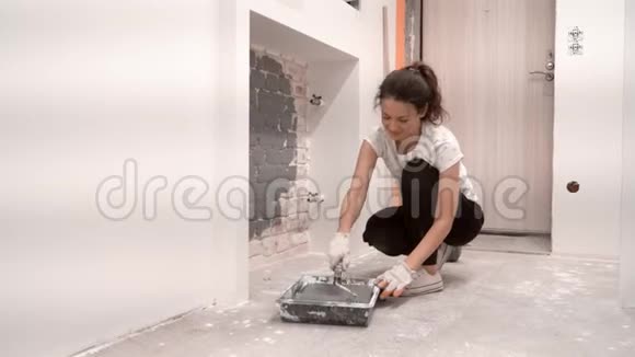 蹲着的女人滚出油漆滚筒用灰色油漆砖墙视频的预览图