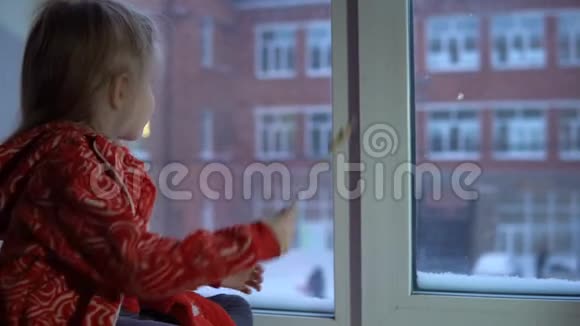 小可爱的女孩坐在窗台上望着外面的雪城风景视频的预览图