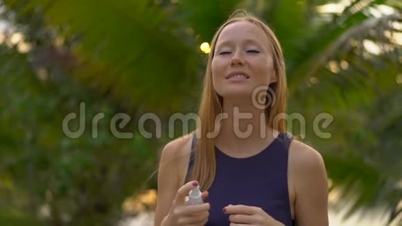 一位美丽的年轻女子用防蚊剂喷在皮肤上的超慢镜头一片热带视频的预览图