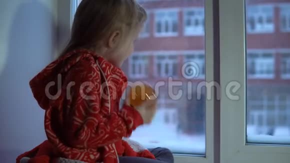 小可爱的女孩坐在窗台上望着外面的雪城风景视频的预览图