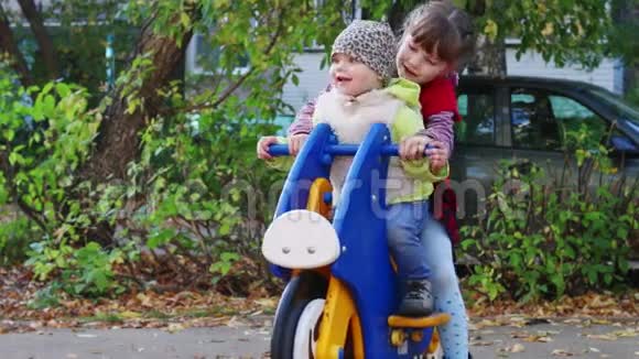 女孩骑着木制摩托车和姐姐在操场上玩耍视频的预览图