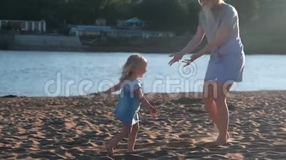 妈妈和女孩在日落时在河的海滩上玩耍视频的预览图