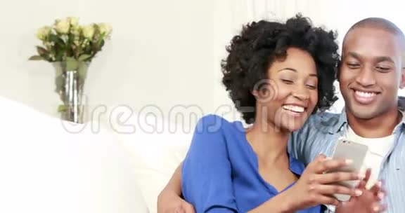 幸福的年轻夫妇坐在沙发上而女朋友正在发短信视频的预览图
