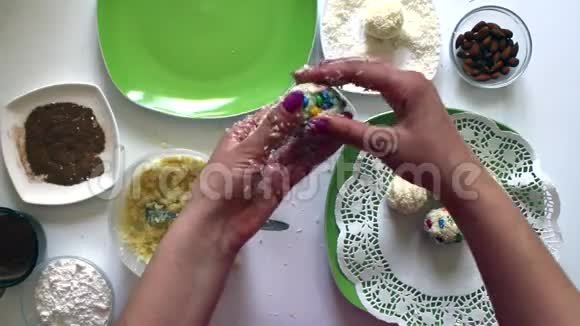 女人用炼乳椰子刨花和杏仁准备糖果用彩釉装饰糖果视频的预览图