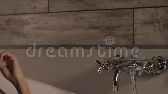 美丽的女人躺在白色的浴缸里梦想着触摸头发视频的预览图