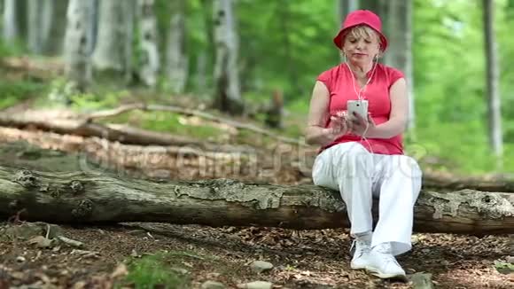 女人坐在森林中的一棵倒下的树上用智能手机视频的预览图