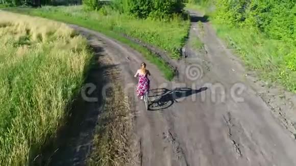 穿裙子的女孩和一个孩子骑着自行车沿着麦田用无人机射击从美丽的风景视频的预览图