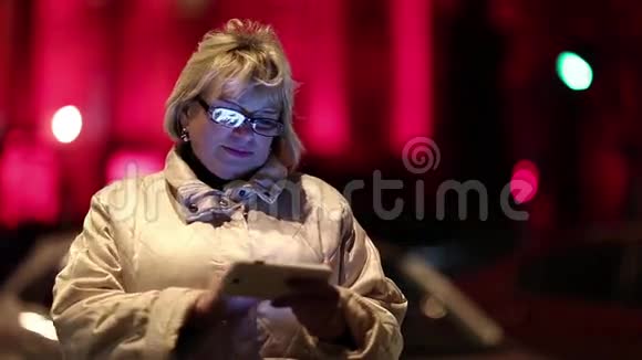 夜间一位拥有智能手机的老妇人站在路边视频的预览图