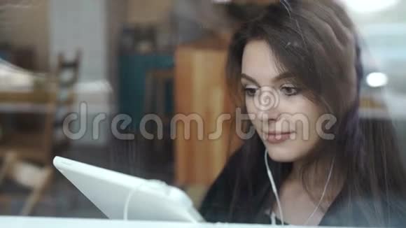 一位年轻女士在咖啡店用带耳机的平板电脑视频的预览图