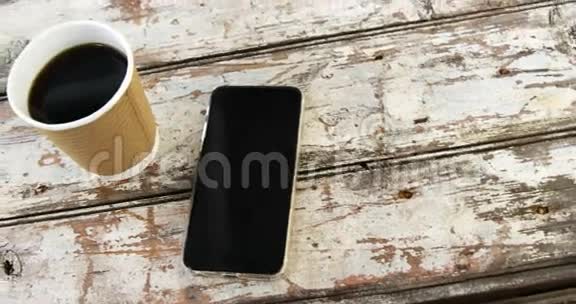 木制木板上的一次性咖啡杯和手机视频的预览图