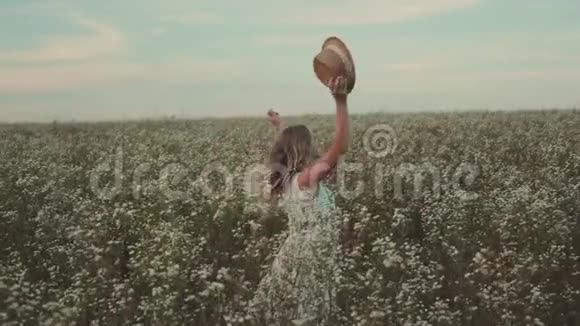 一个手拿帽子的女孩在一片开着野花的田野里散步视频的预览图
