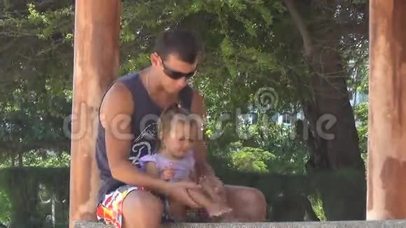 爸爸和宝宝在海边的凉亭里玩女孩踩着脚爸爸保留女儿的腿他们在笑视频的预览图