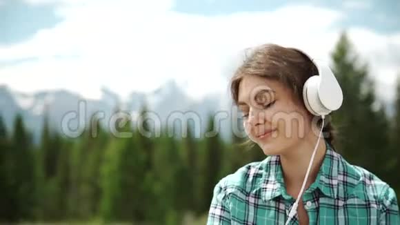 休闲的女孩听着音乐坐着在夕阳下的绿色田野里放松视频的预览图