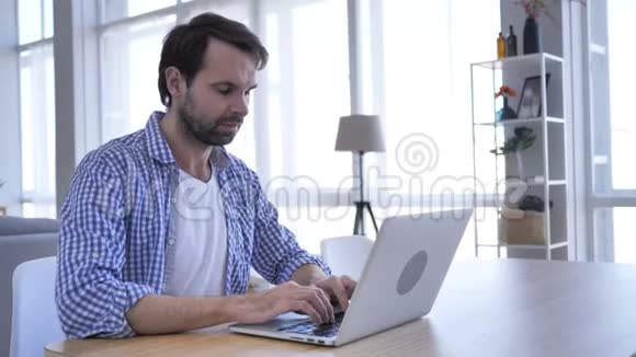 办公室里用笔记本电脑工作的漫不经心的胡子男人特写视频的预览图