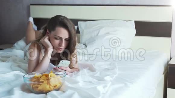 女孩在床上吃薯条在电话里看新闻视频的预览图