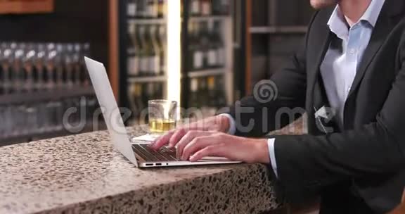 微笑的商人喝酒时在他的笔记本电脑上打字视频的预览图