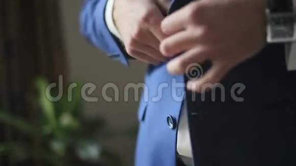 年轻的帅哥穿着时髦的蓝色西装在他的夹克上扣纽扣视频的预览图