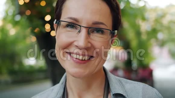 戴着眼镜面带笑容在户外看镜头的开朗黑发女人的肖像视频的预览图
