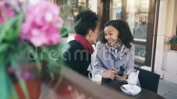 两个有魅力的混血女朋友在户外街头咖啡馆用智能手机分享视频的预览图