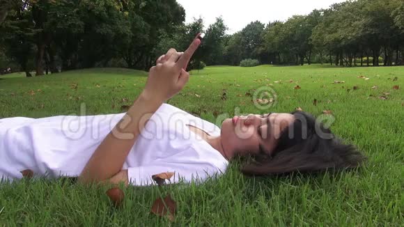 年轻女子躺在草地上发短信在公园里发短信视频的预览图