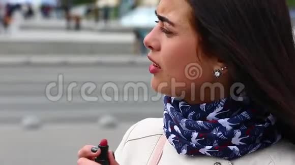 年轻女士一边看着镜子一边在大街上嘴唇涂红唇膏视频的预览图