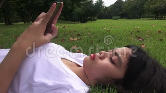 高清格式年轻女子躺在草地上发短信在公园发短信视频的预览图