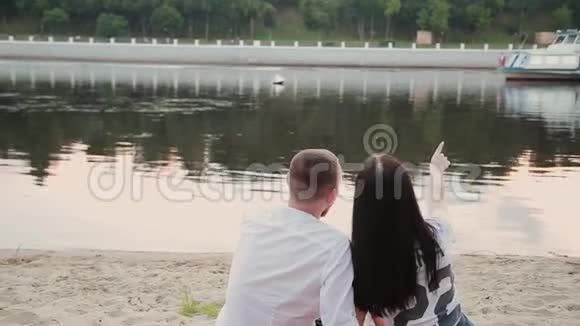 可爱的夫妇坐在海滩上拥抱日落视频的预览图