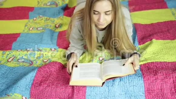漂亮的年轻女人在家里的床上看书在家学习视频的预览图