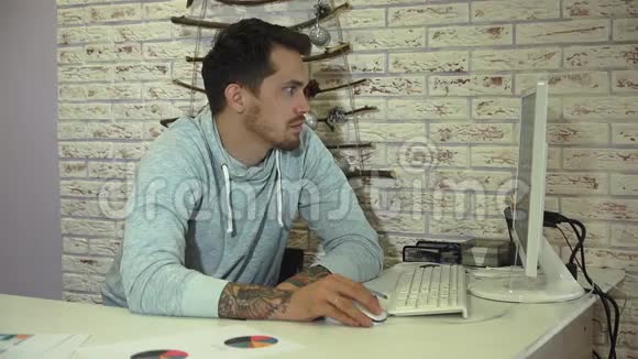 年轻的胡子商人穿着灰色运动衫在明亮的办公室工作视频的预览图