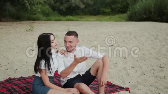 可爱的夫妇坐在海滩上拥抱日落视频的预览图
