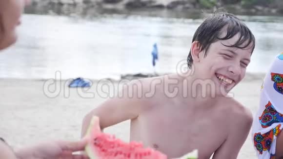 孩子们青少年在海滩上休息笑着吃西瓜慢动作视频男孩和女孩休息视频的预览图