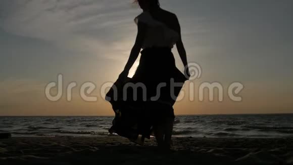 日落时分一个女人在海滩上跳舞的剪影飞行裙视频的预览图