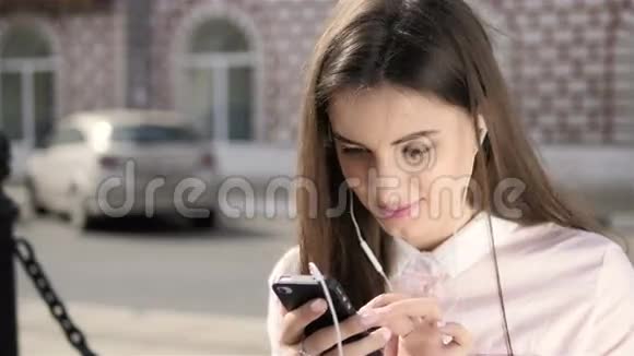 年轻时尚漂亮的女孩与电话摆在城市街道青少年模型有耳机视频的预览图