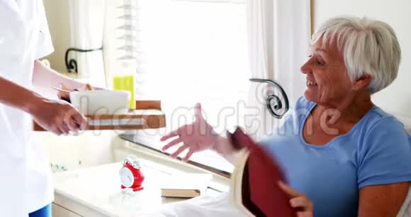 女医生在卧室里为老年妇女提供早餐视频的预览图