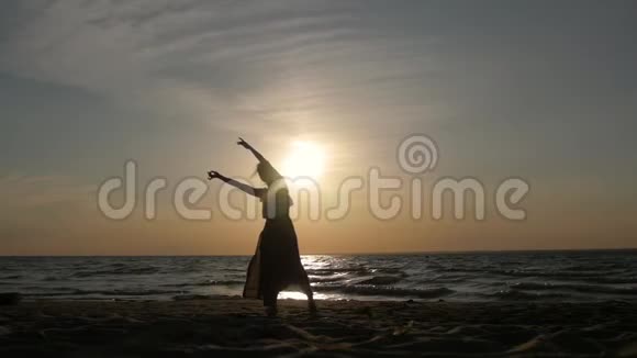 日落时分一个女人在海滩上跳舞的剪影空中飞裙视频的预览图