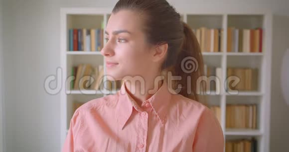 一位年轻可爱的女学生在学院图书馆里用书架开心地看着镜头的特写镜头视频的预览图